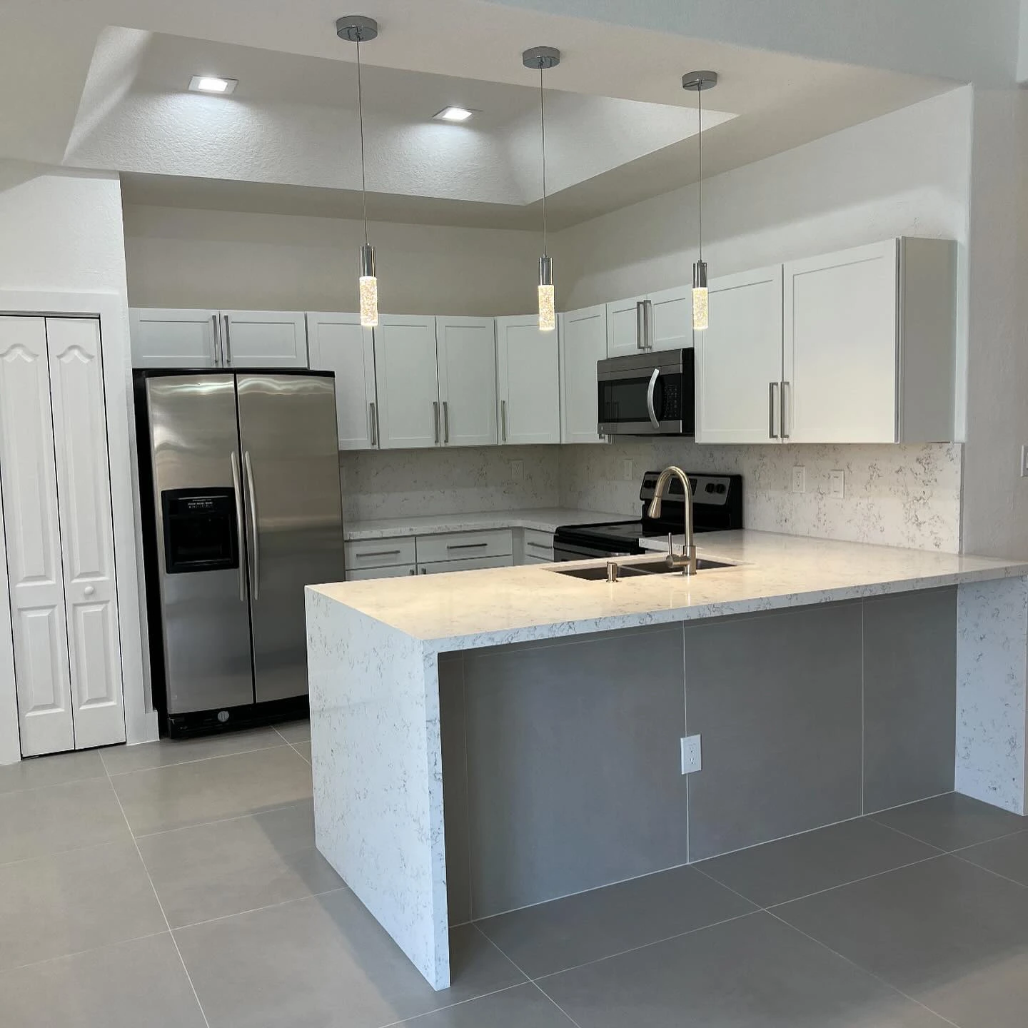 Completed kitchen remodel with white cabinetry, pendant lighting, and a waterfall breakfast bar, from our Instagram project